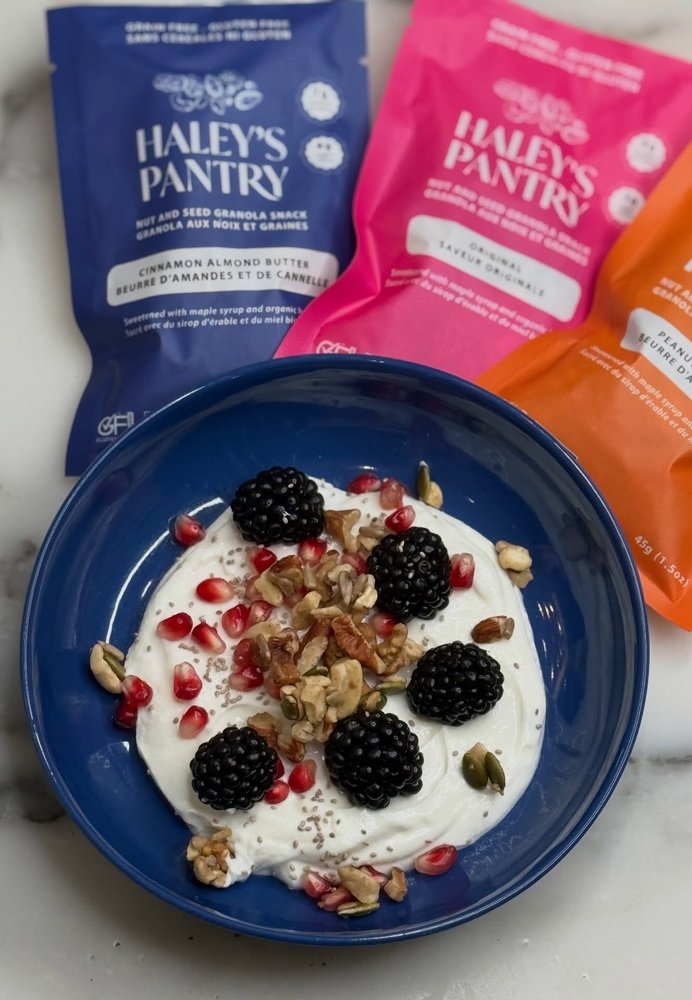Yogurt bowl topped with granola and fresh berries beside Haley's Pantry snack packs
